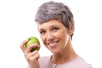 Woman with an implant denture in Temple holding an apple